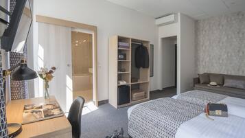 A hotel room with a desk, a chair, a bed with a patterned bedspread, a wardrobe, and a small table with a vase of flowers.