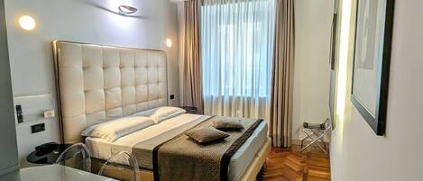 Quarto com teto de madeira, cama com cabeceira, mesa de cabeceira, uma cadeira e janela com cortinas.