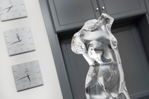 Escultura d'una figura humana realitzada amb un material reflectant, amb rellotges que mostren l'hora de Nova York, Roma i Londres.
