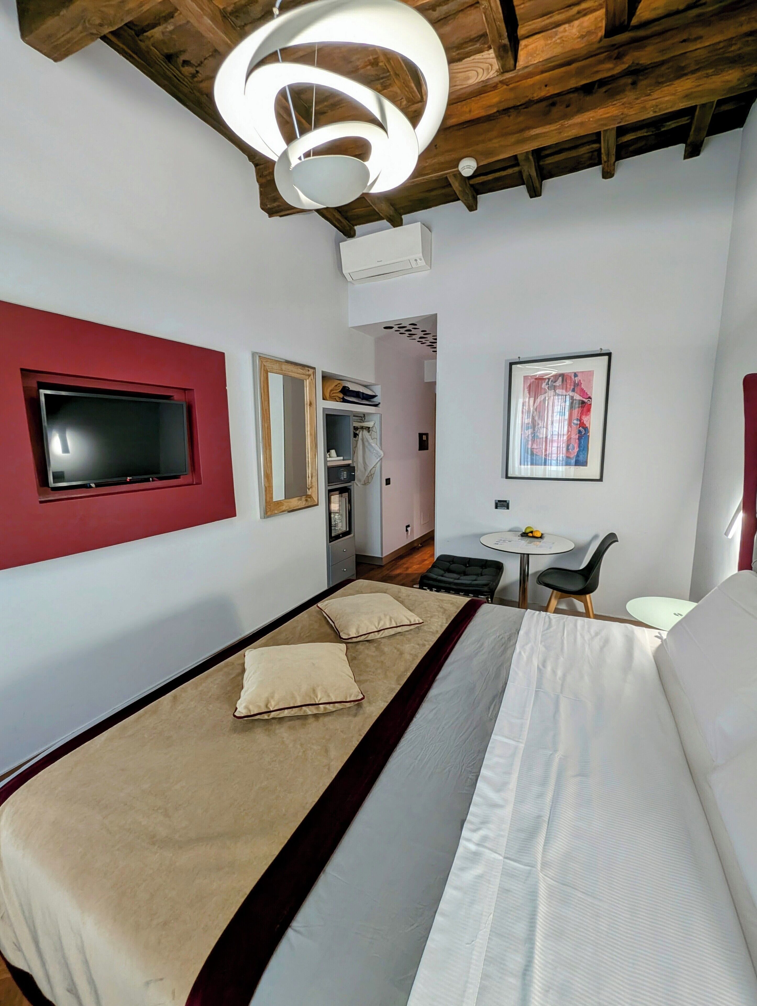 A hotel room with a bed, a TV mounted on the wall, a desk with a chair, and a framed picture on the wall.
