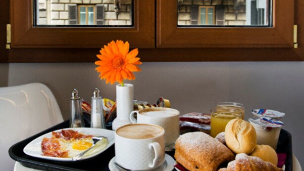 A breakfast tray with croissants, pastries, and a coffee cup on a table by a window with a view of buildings. - Relais Forus Inn (Rome)