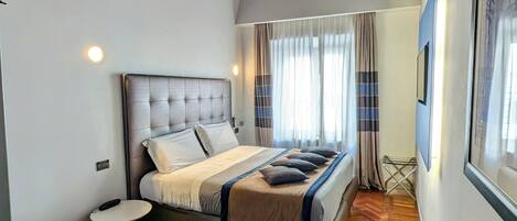 A bedroom with a bed, a desk with a chair, a window with curtains, and a wooden ceiling.