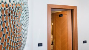A wooden door with a number plate indicating room 107, a wall-mounted light switch, and a patterned wall feature. - Relais Forus Inn (Rome)