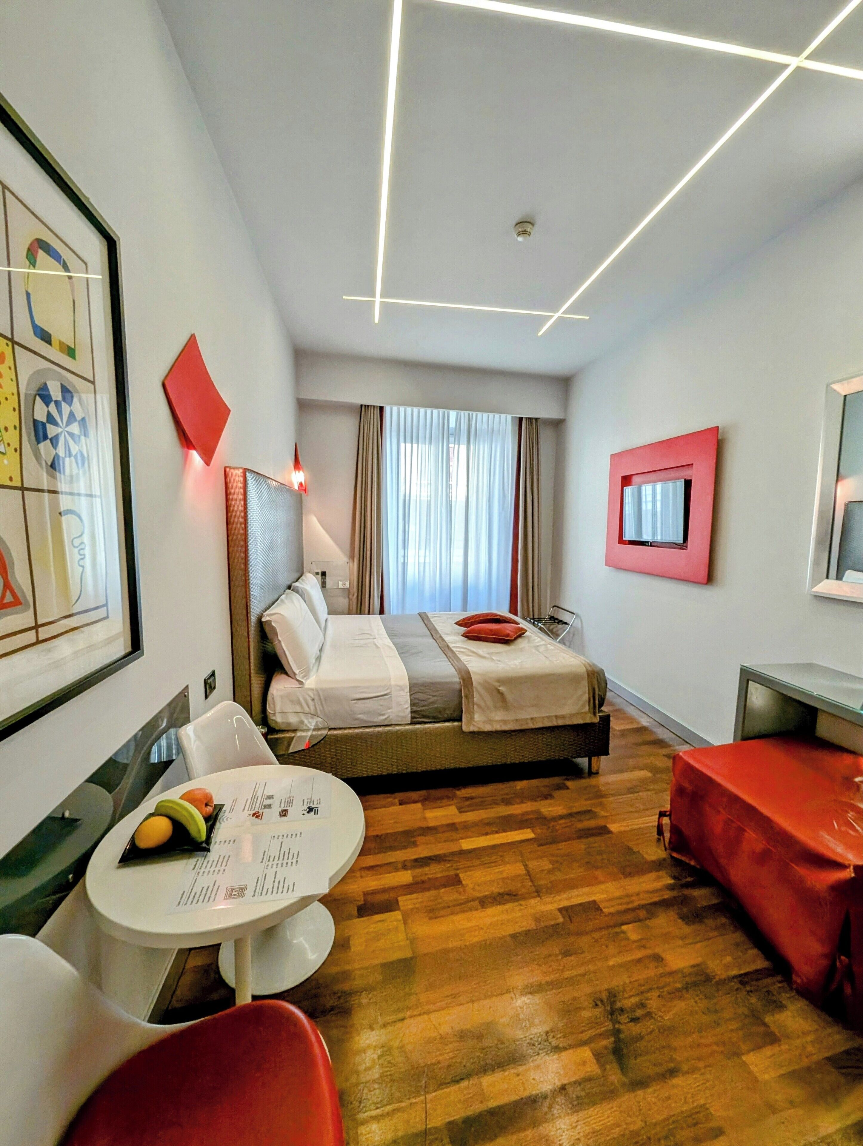 A modern hotel room with a bed, a desk, a chair, a small table with fruit, and a television.