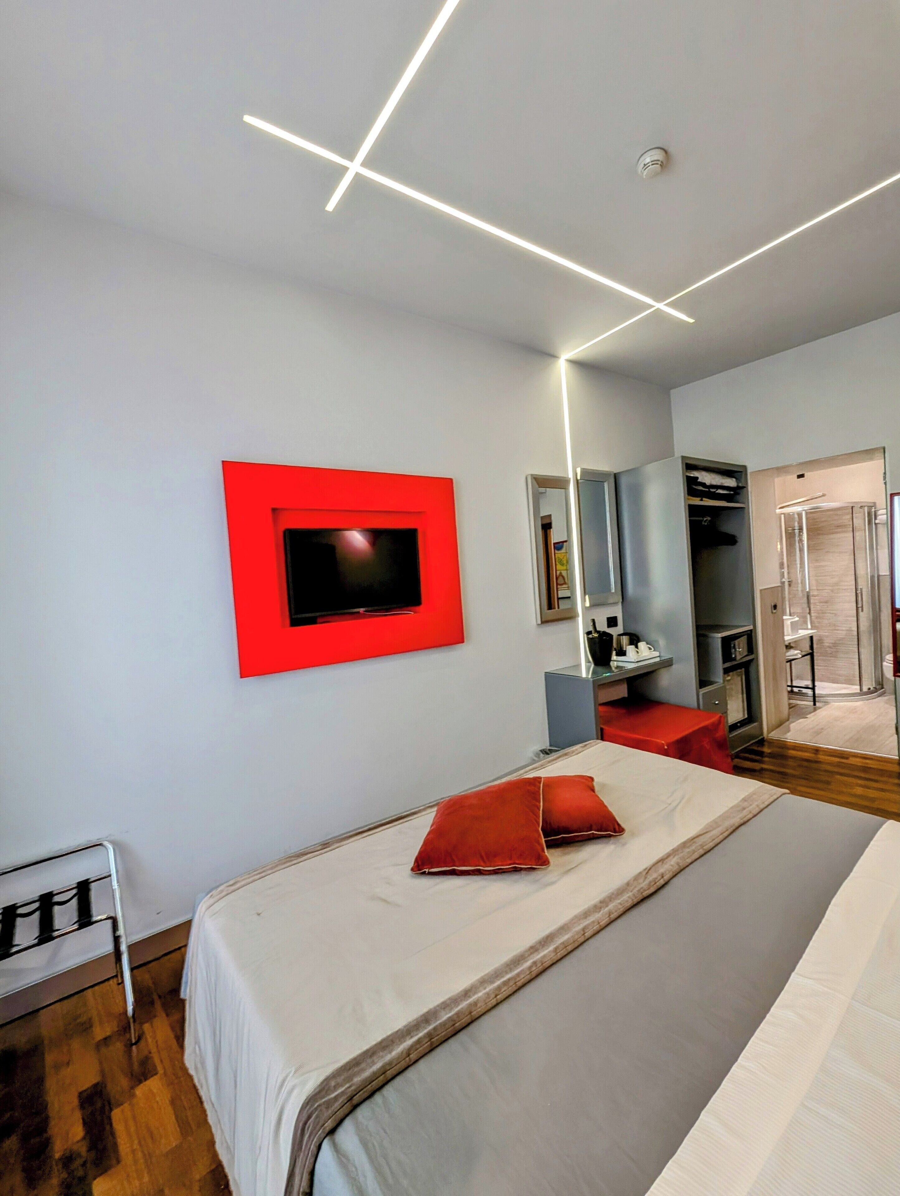 Una camera d'albergo moderna con un letto grande, una TV a parete, un armadio e un bagno visibile attraverso una porta aperta.
