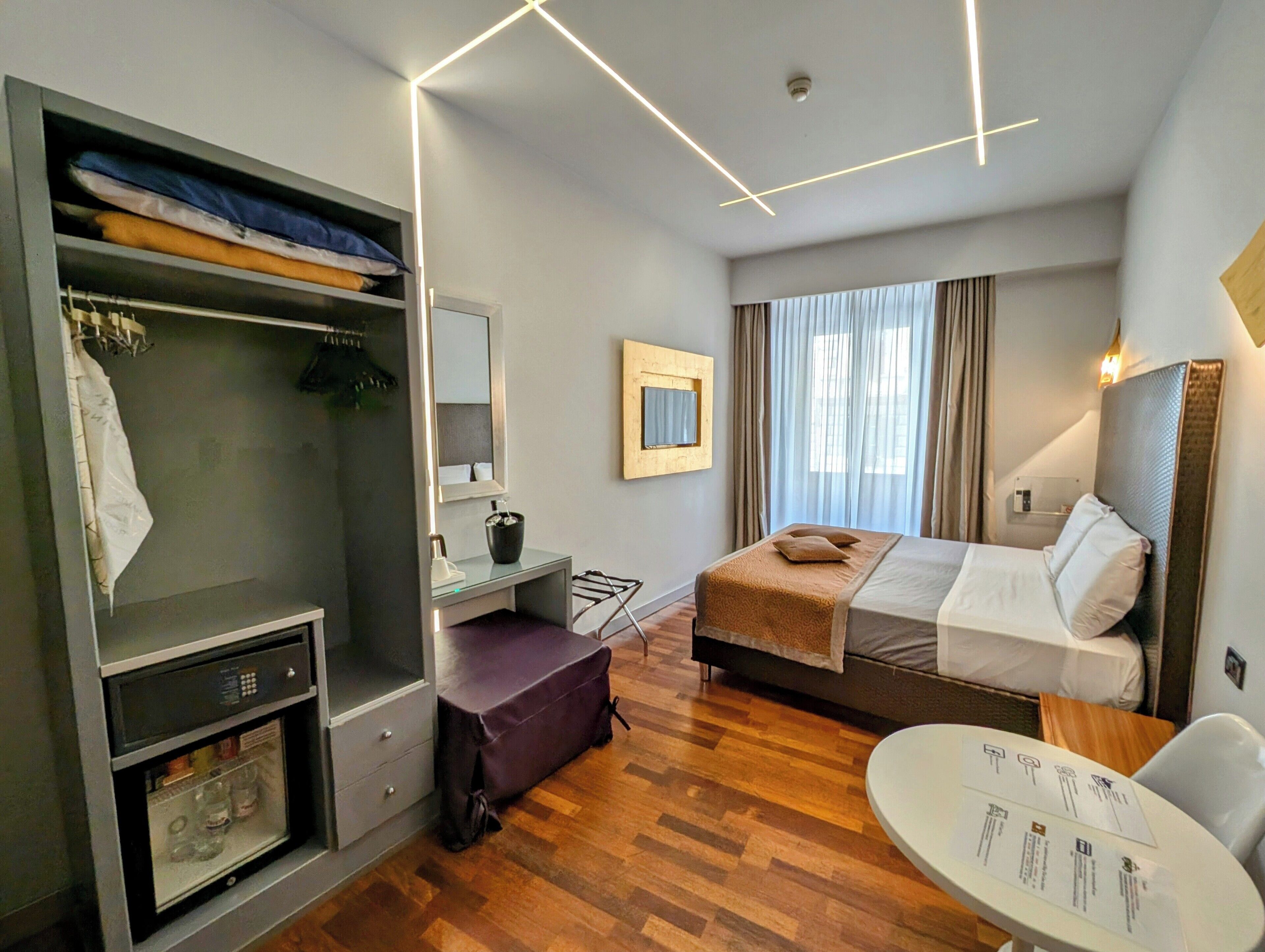 A modern hotel room with a bed, a desk, a wardrobe, and a seating area.