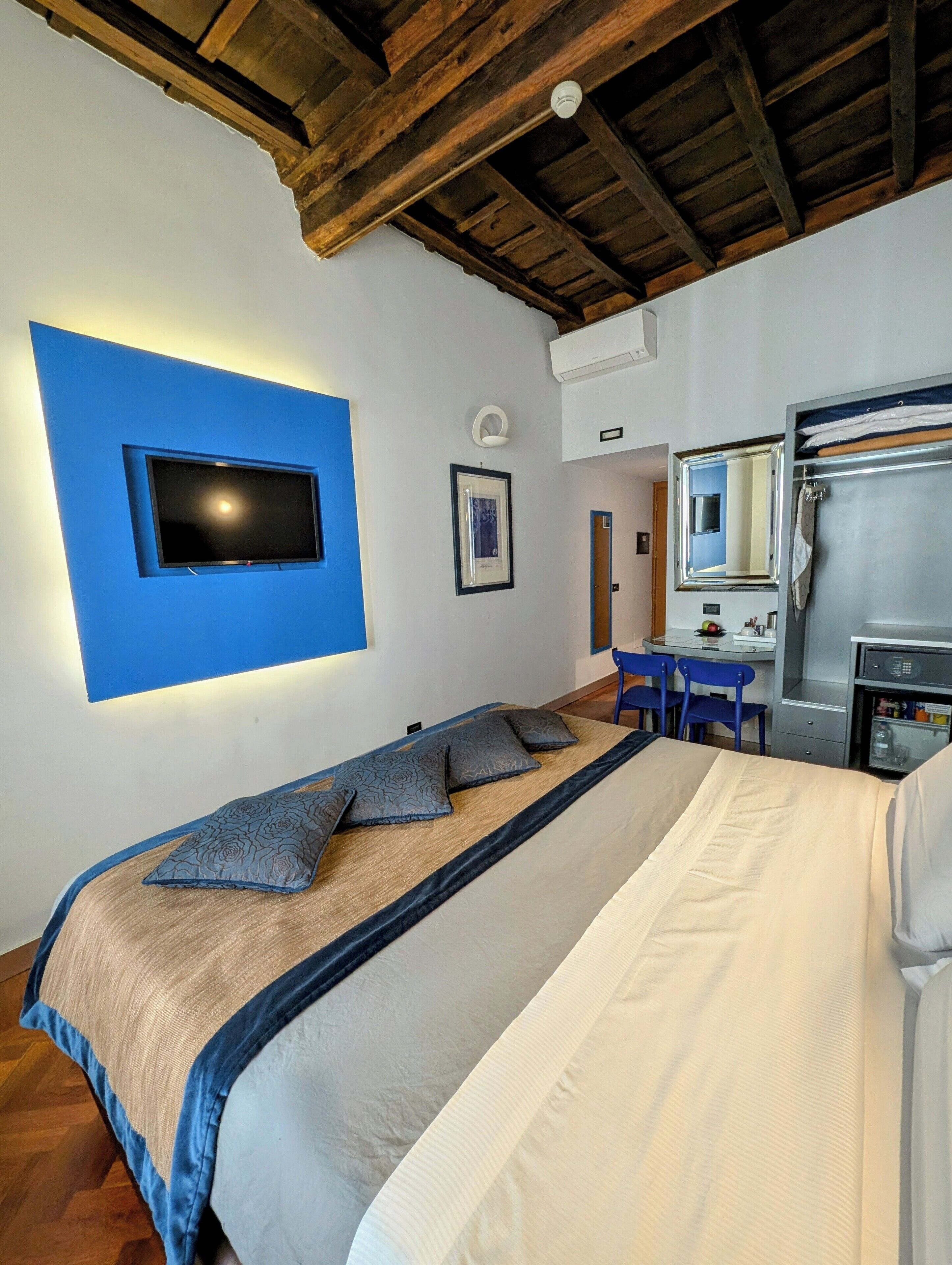Une chambre à coucher avec un lit, un téléviseur fixé au mur, un bureau avec une chaise et un miroir.