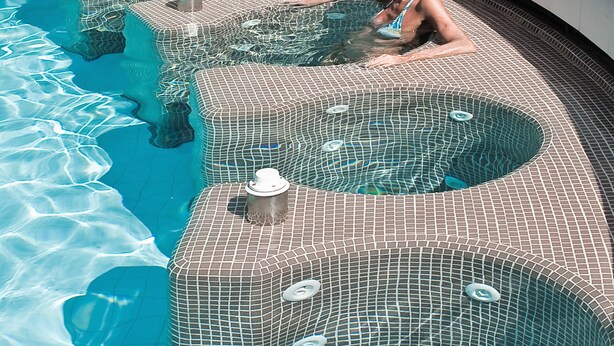 Una piscina con un diseño de mosaicos único y una persona relajándose en el agua.