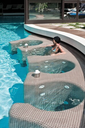Une piscine dotée d’un revêtement de carrelage original et une personne se relaxant dans l’eau.