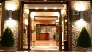 Entrada de hotel con puerta de madera, paredes de piedra y plantas en macetas.