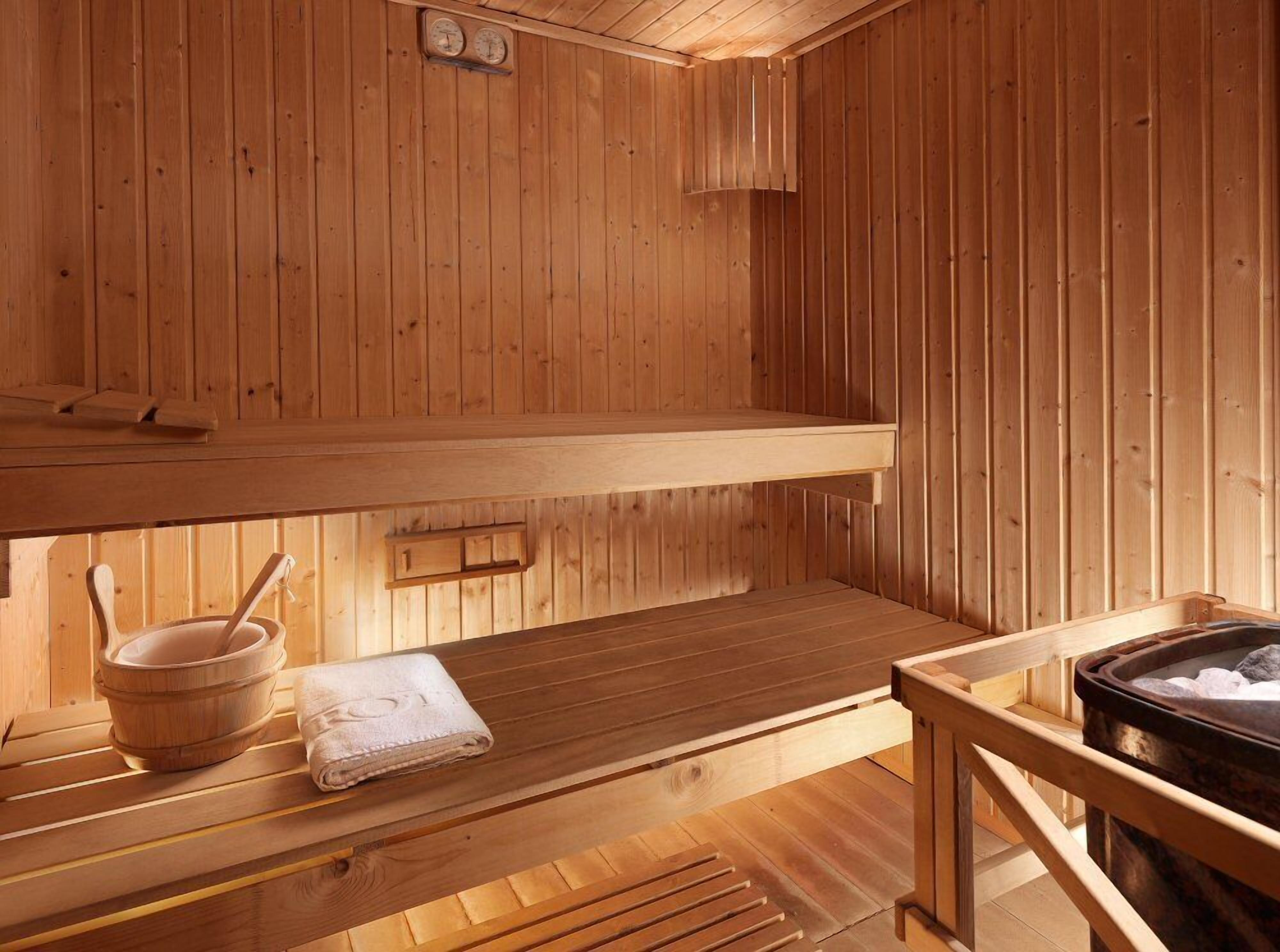 A wooden sauna with benches, a wooden basin, and a towel.