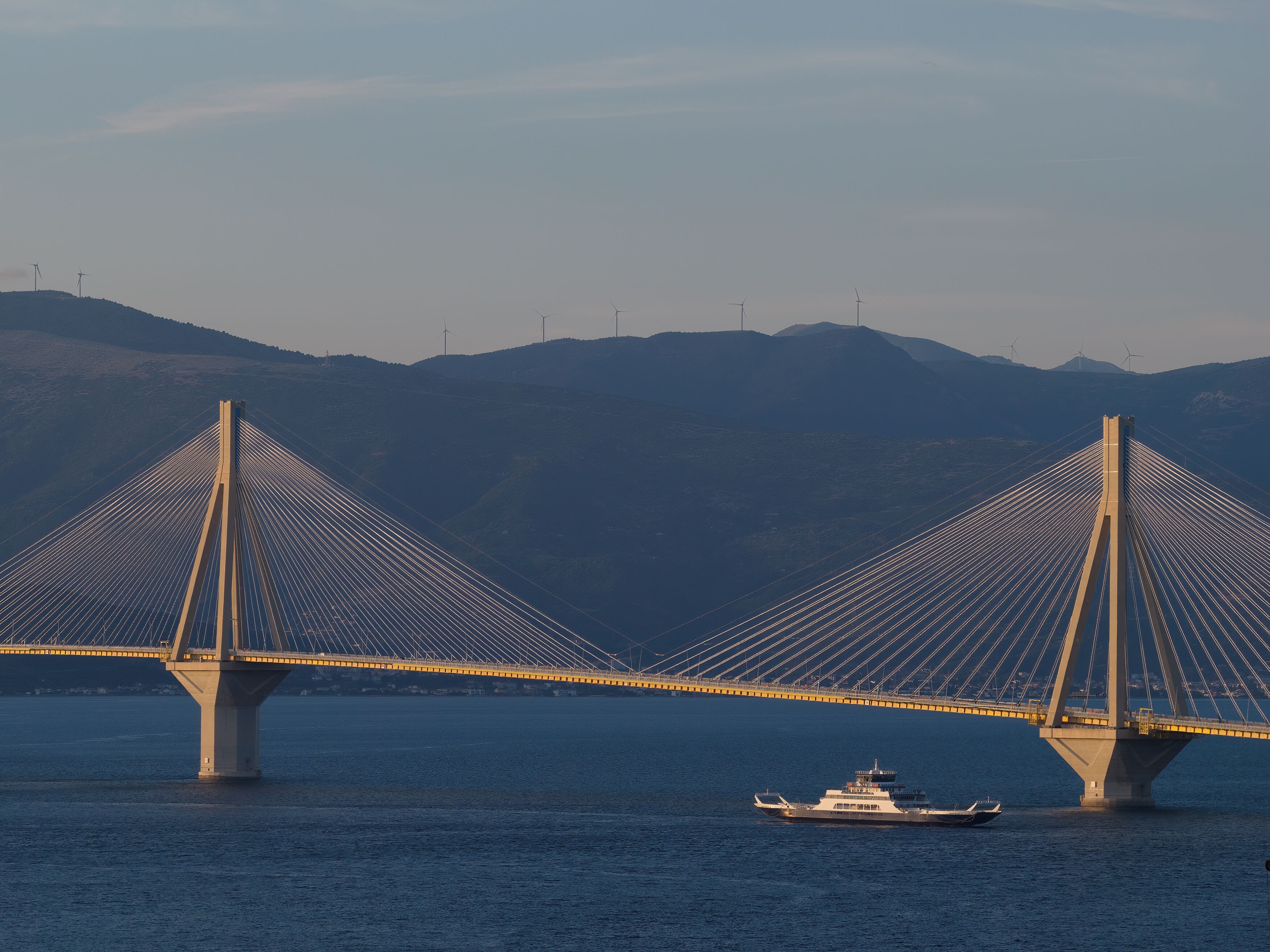 A large suspension bridge with two main towers and cables, spanning over a body of water with a boat in the foreground.