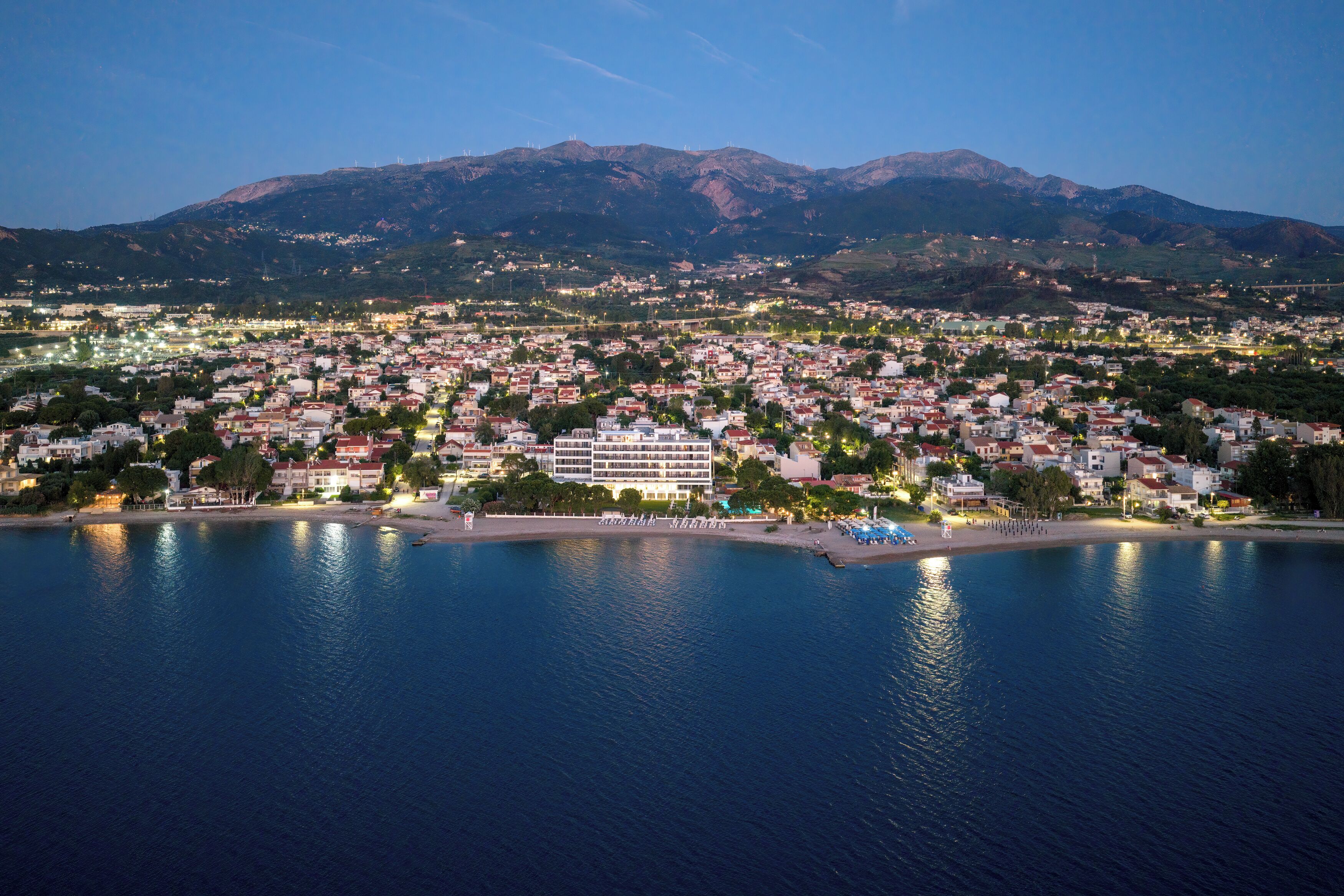 Une ville côtière qui abrite un hôtel imposant, doté de plusieurs étages, situé en bord de mer, avec des montagnes en toile de fond.