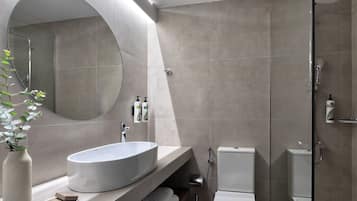 Ein modernes Badezimmer mit einem großen, ovalen Waschbecken, einem runden Spiegel, einer Duschkabine und einer Toilette.