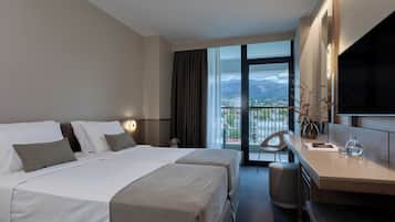Habitación de hotel con dos camas, un escritorio, una silla, un televisor y un balcón con vistas a la montaña.