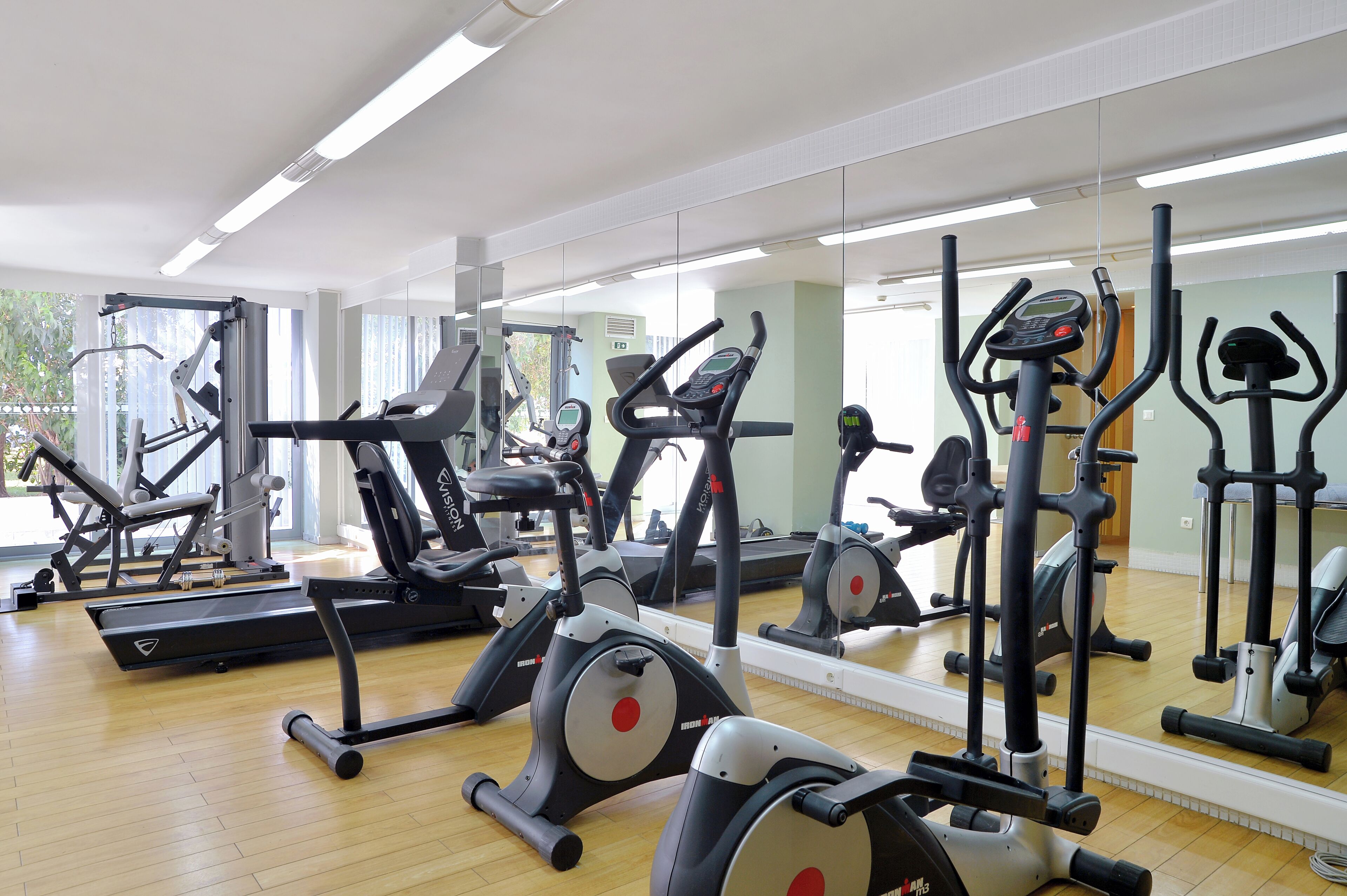 Un gimnasio con varias máquinas de ejercicio, espejos grandes y suelo de madera.