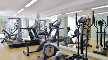 A gym with various exercise machines, large mirrors, and a wooden floor.