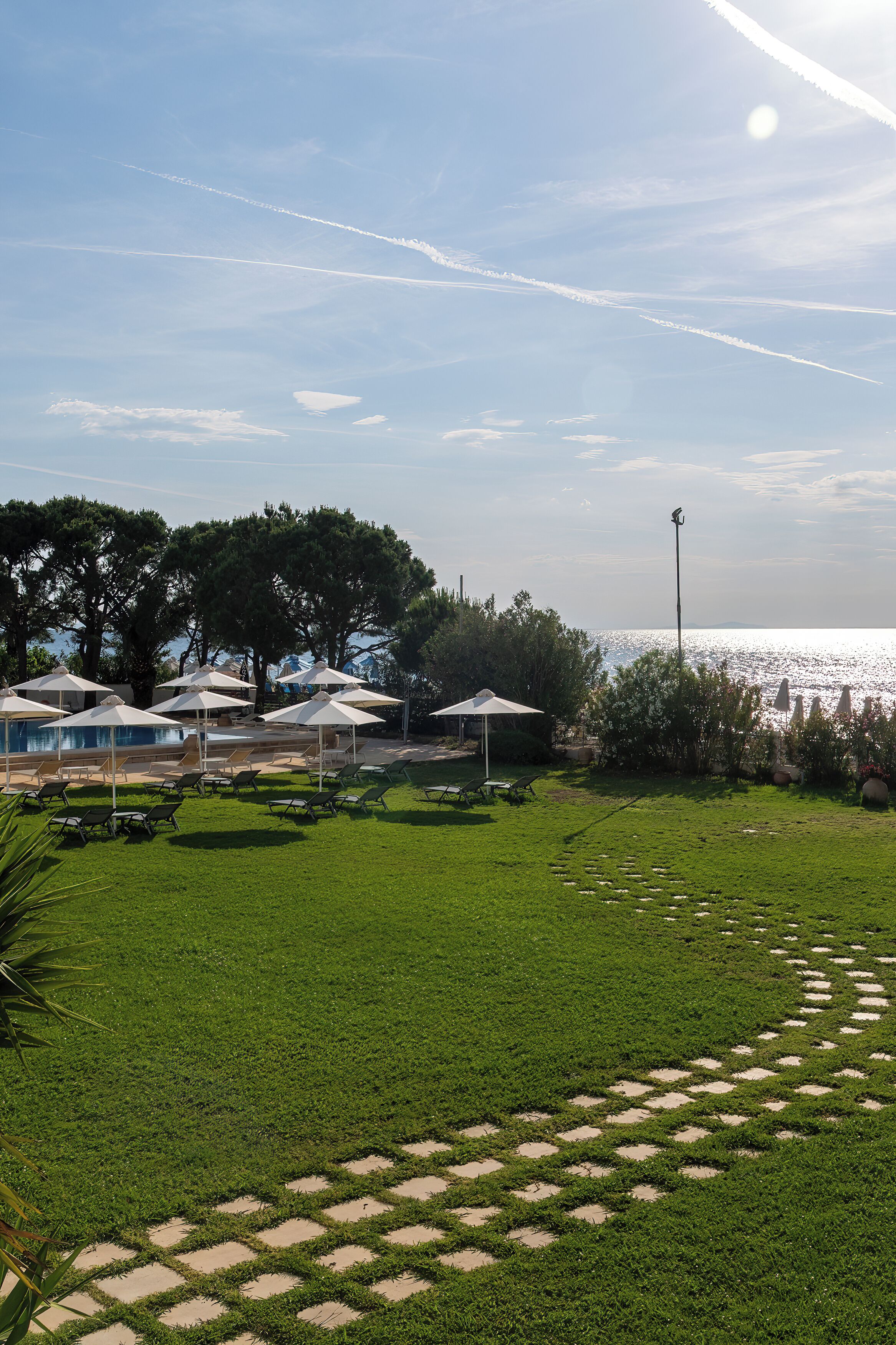 Ein Poolbereich mit Sonnenschirmen, Liegestühlen und Blick auf das Meer.