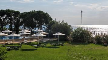 A pool area with umbrellas, lounge chairs, and a view of the sea.