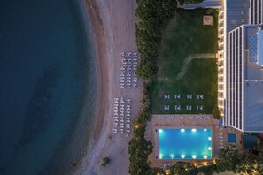 An aerial view of a hotel with a swimming pool, beachside lounge chairs, and a well-maintained lawn.