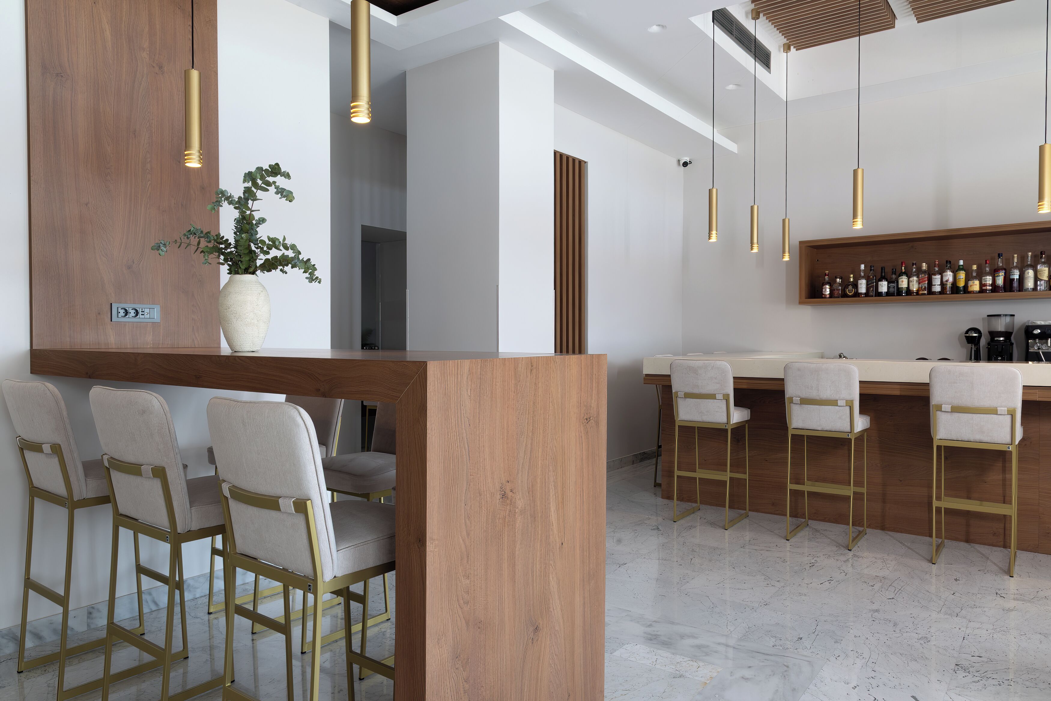 A bar area with wooden accents, bar stools, and hanging pendant lights.