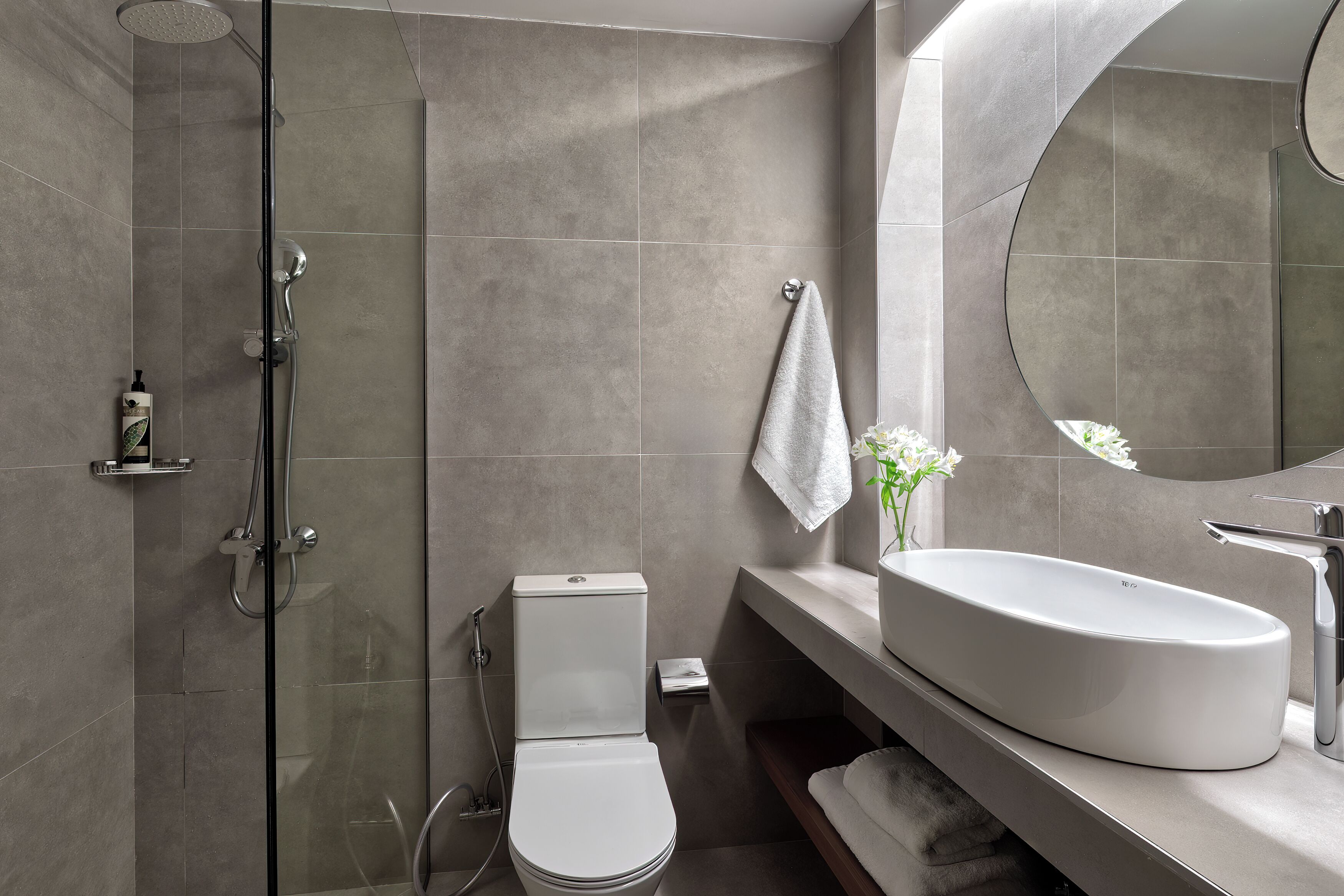 A modern bathroom with a glass-enclosed shower, a white toilet, a large sink, and a mirror.