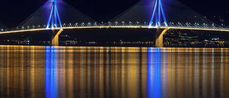 Une vue nocturne d’un grand pont suspendu, avec deux hautes tours et des câbles, qui enjambe une étendue d’eau, les lumières de la ville scintillant en arrière-plan.