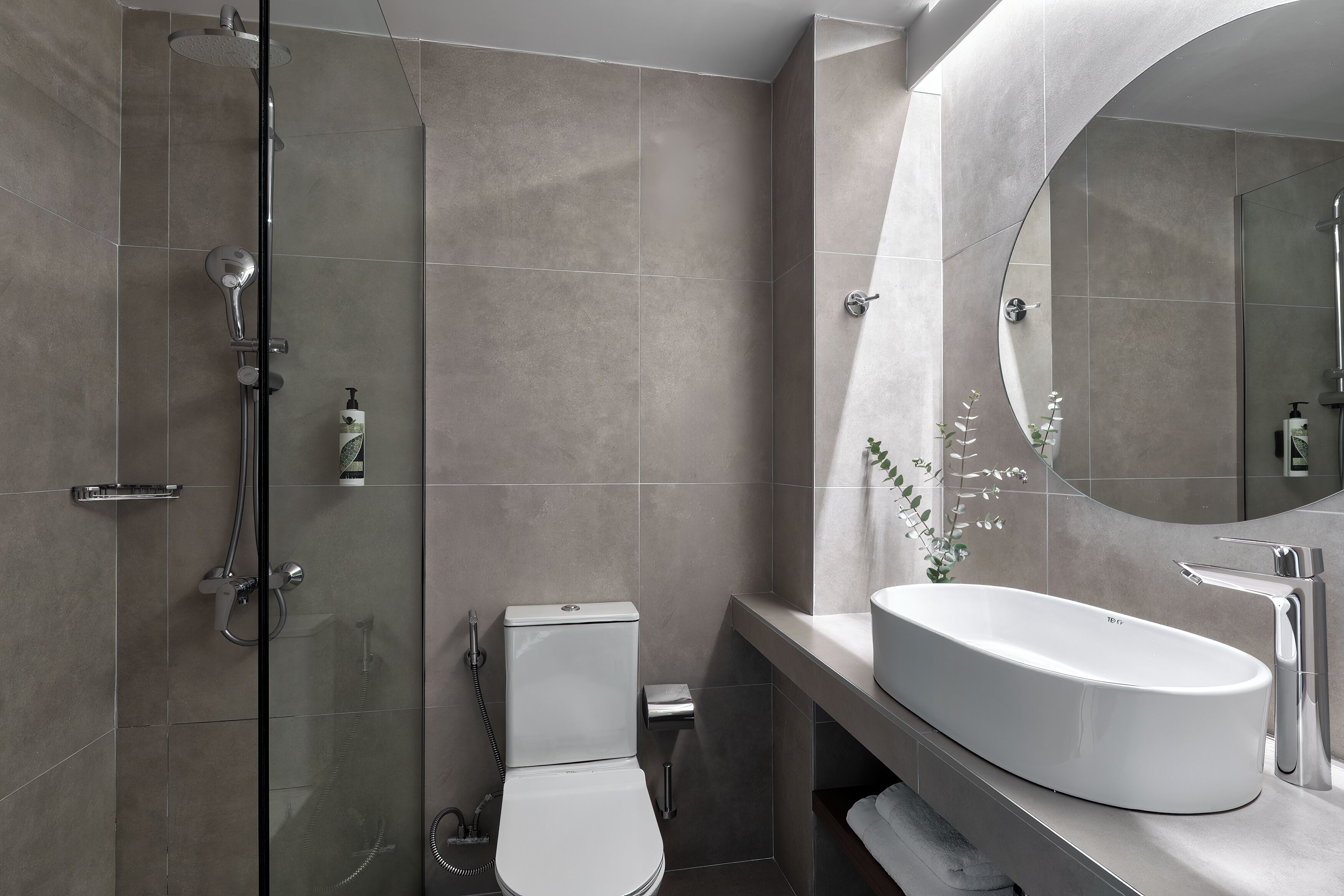 A modern bathroom with a glass-enclosed shower, a white toilet, and a large oval sink with a mirror.