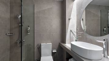 A modern bathroom with a glass-enclosed shower, a white toilet, and a large oval sink with a mirror.