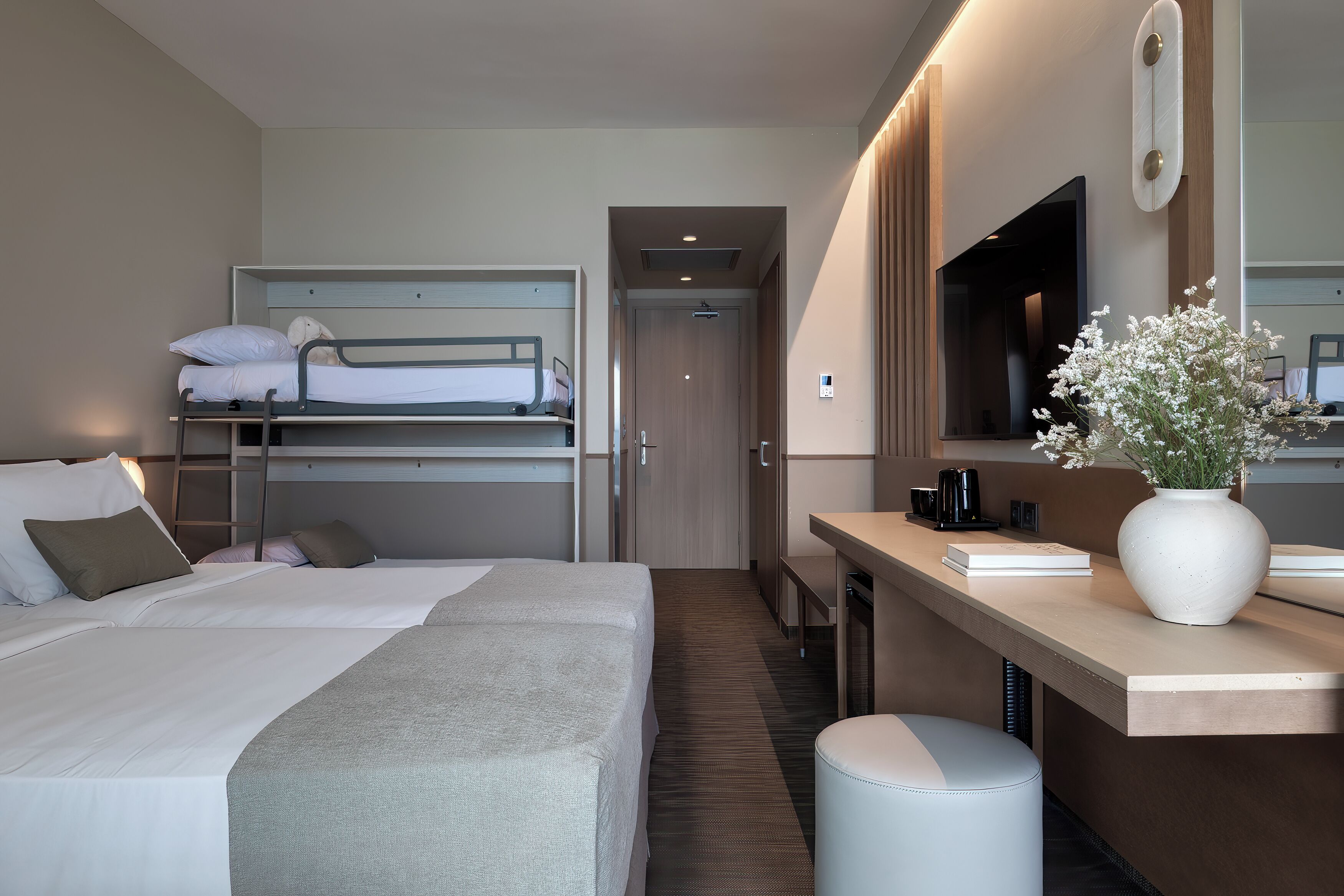 Une chambre d’hôtel avec un lit superposé, un bureau avec un ordinateur, un miroir et un vase avec des fleurs.