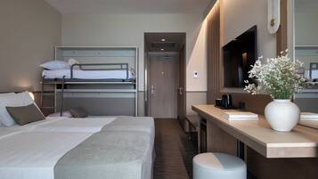 Habitación de hotel con literas, un escritorio con ordenador, un espejo y un florero con flores.