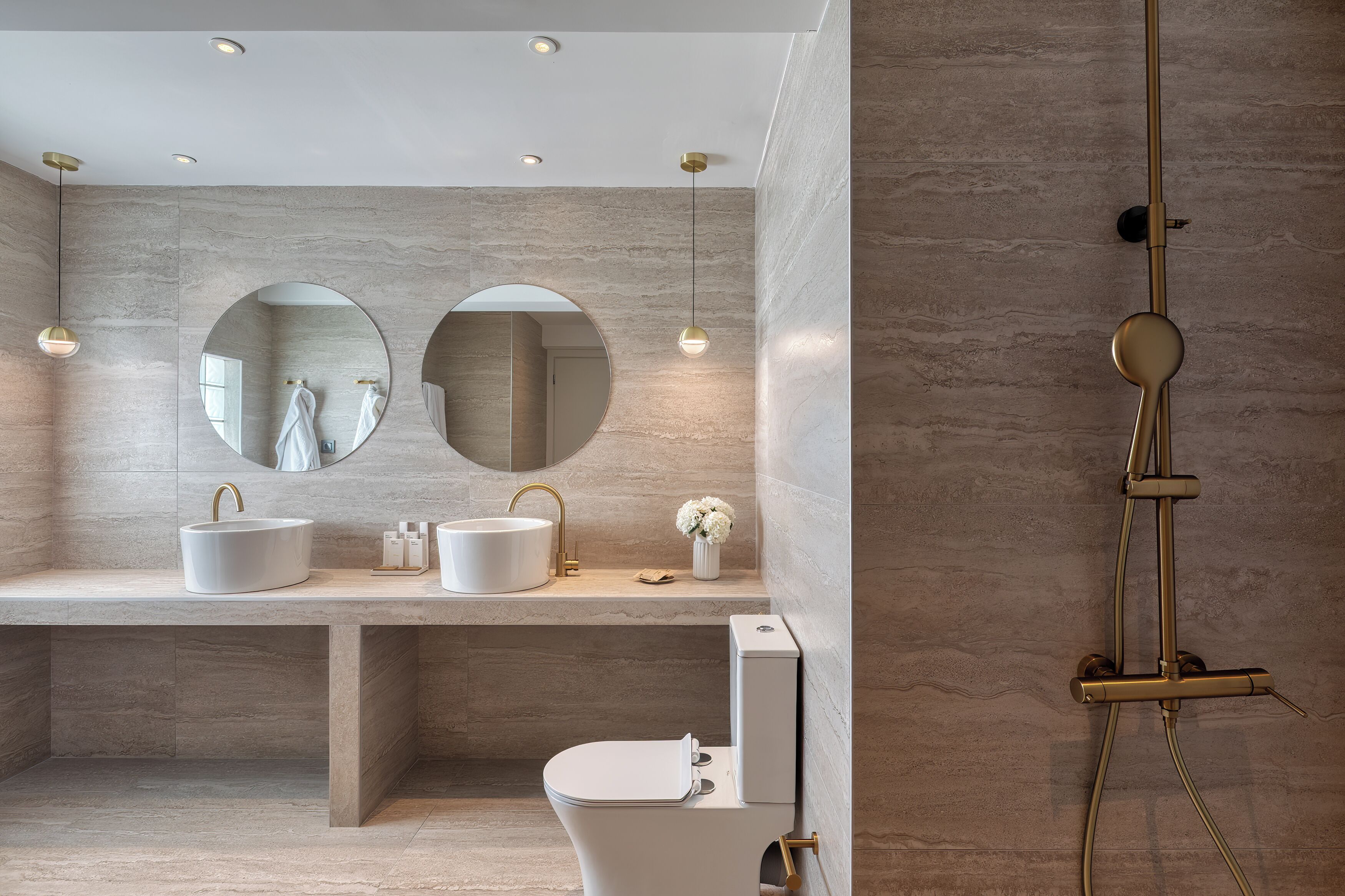 A modern bathroom with a large mirror, two sinks, a toilet, and a shower.