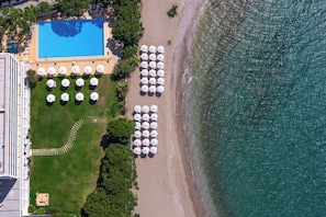 An aerial view of a beach resort with a swimming pool, umbrellas, and a clear view of the ocean.