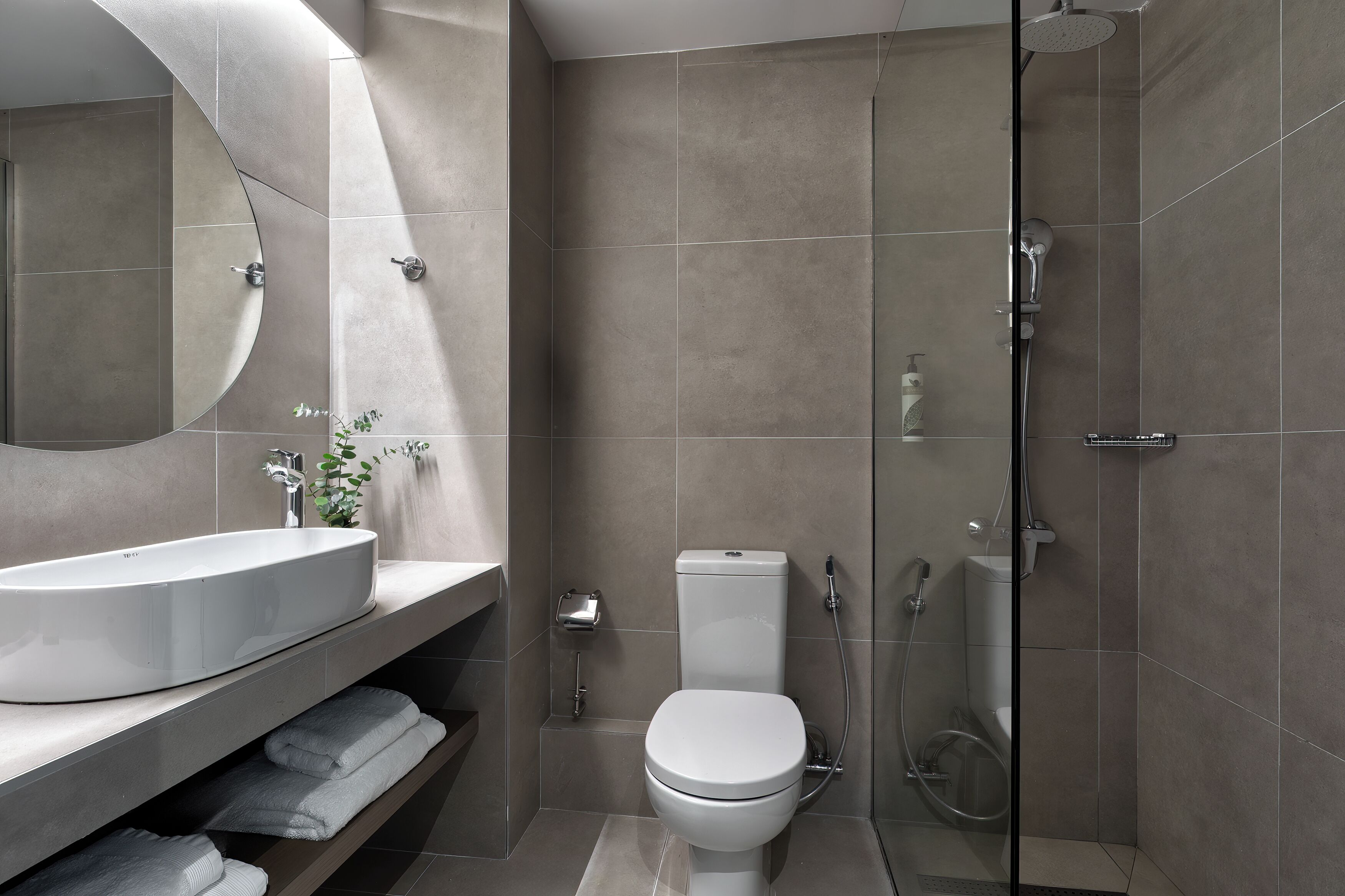 A modern bathroom with a large oval sink, a toilet, and a glass-enclosed shower.