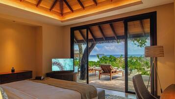 A bedroom with a bed, a television, and a view of the ocean through large sliding doors.