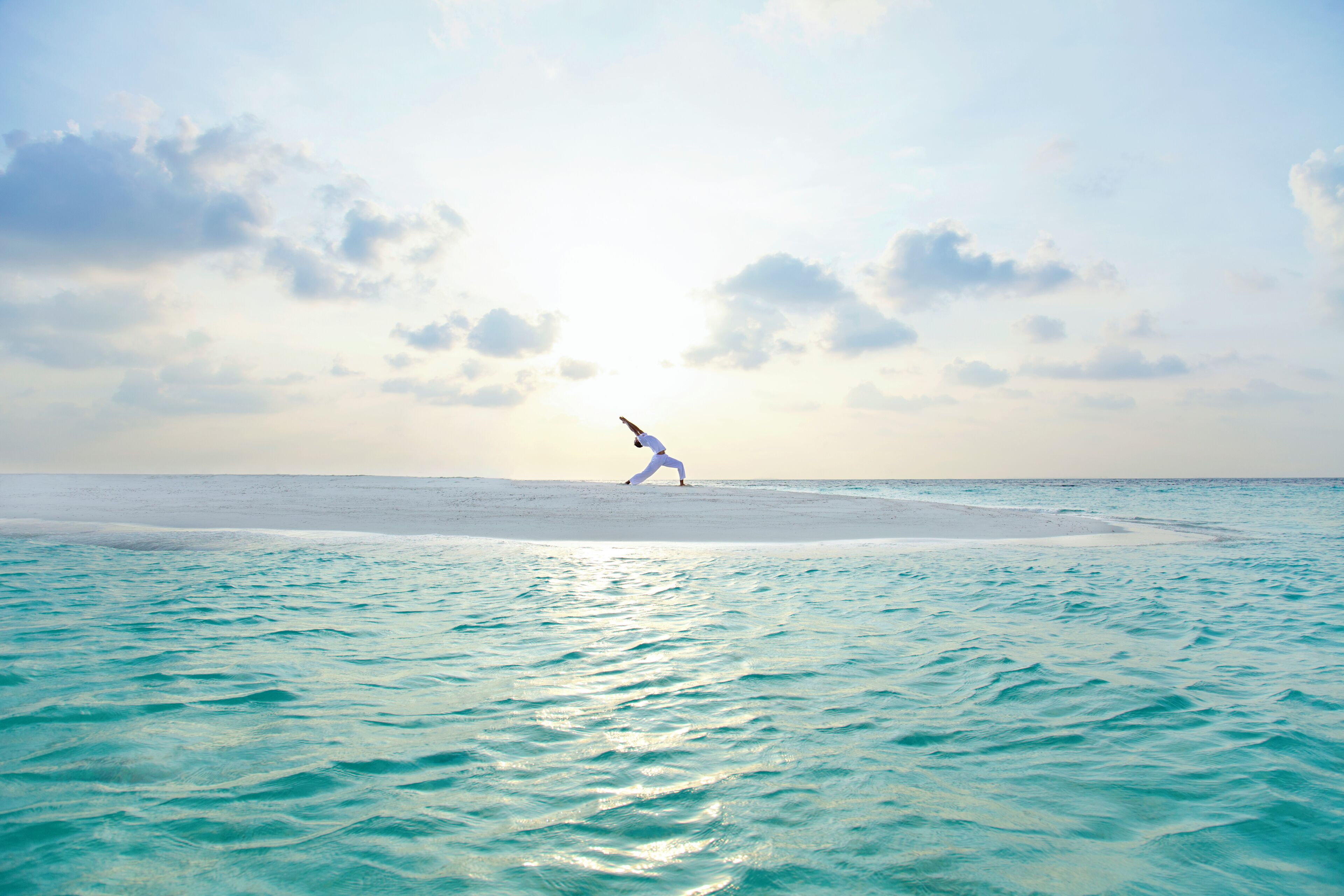 A person in a white outfit on a beach with turquoise water and a clear sky.