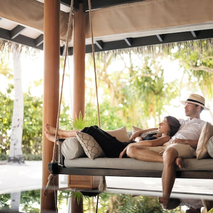 A couple relaxing on a hammock swing with a view of lush greenery.