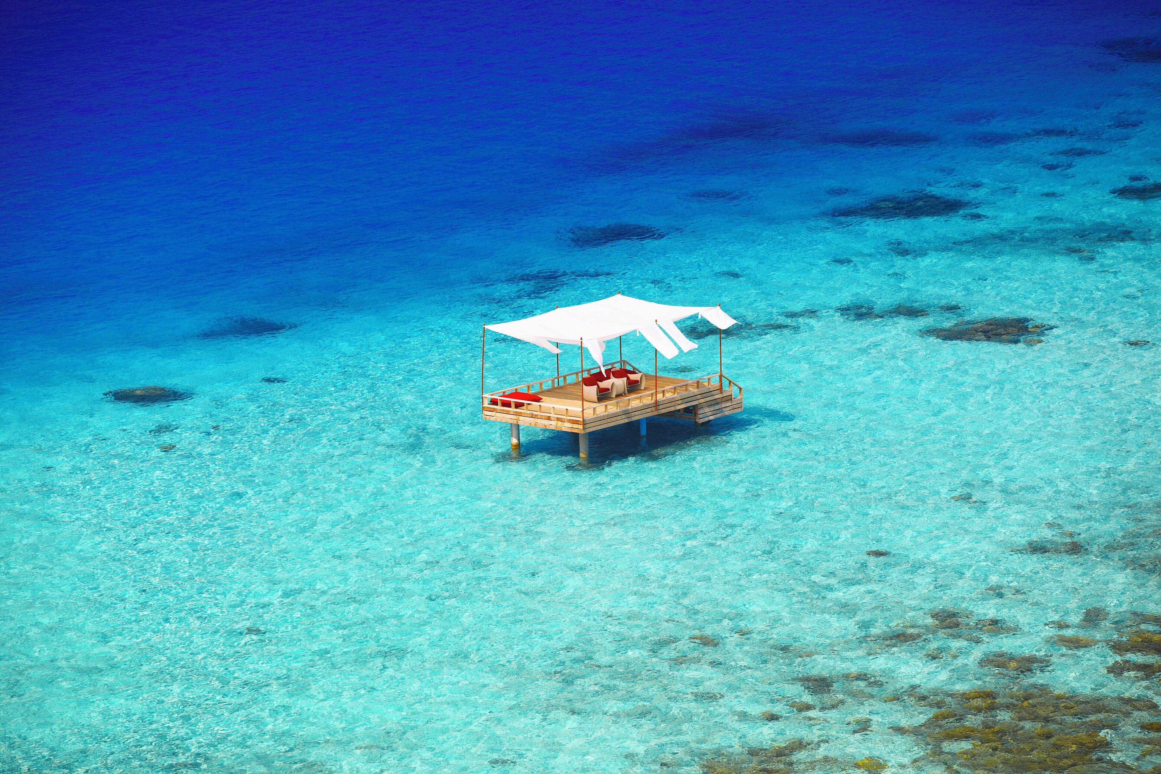 Un bungalow sull'acqua con una tettoia, acqua cristallina e formazioni coralline.