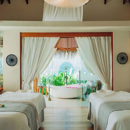 A spa room with two beds, a large bathtub, and a view of greenery outside.