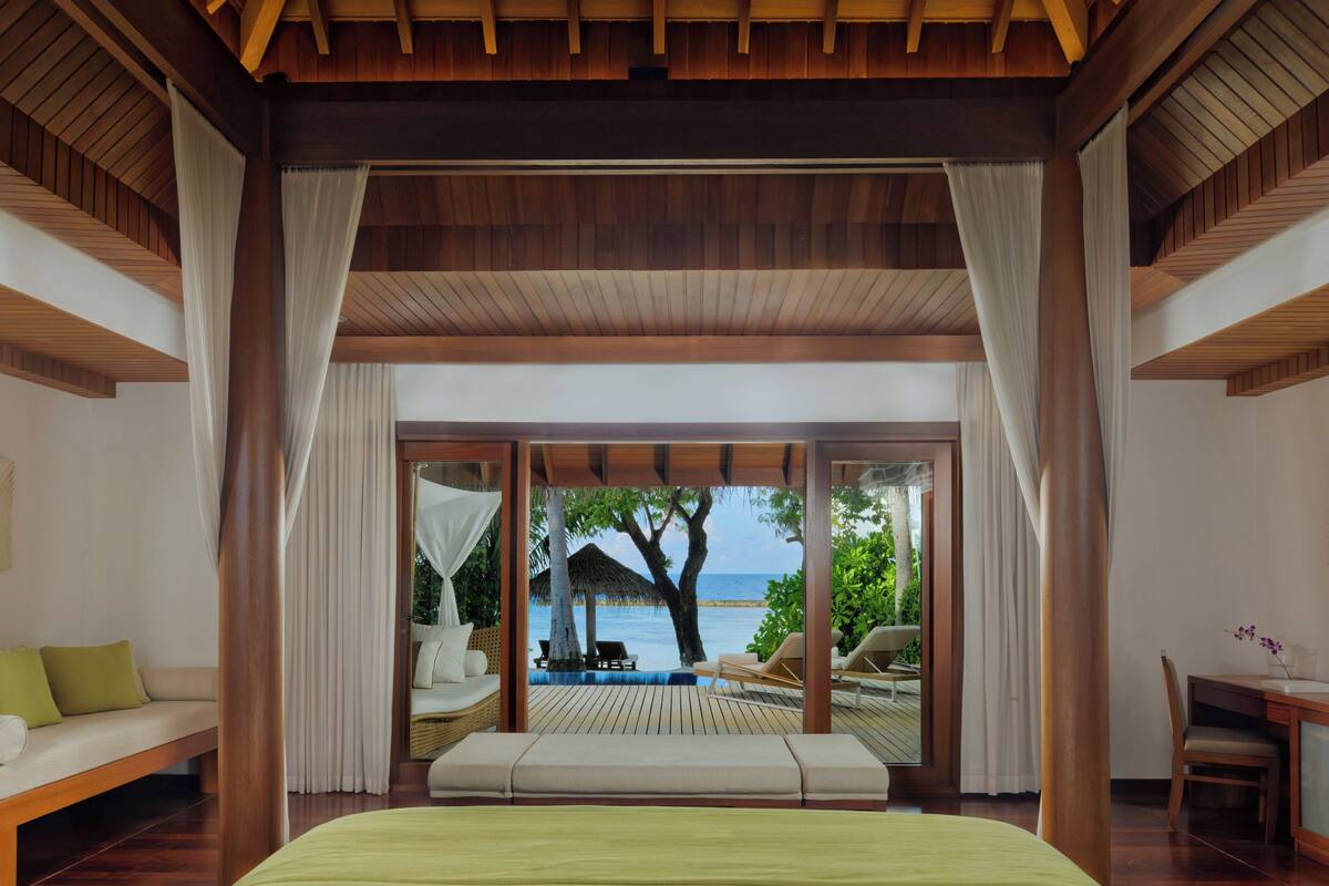 A bedroom with a large bed, a view of the beach, and a wooden ceiling.