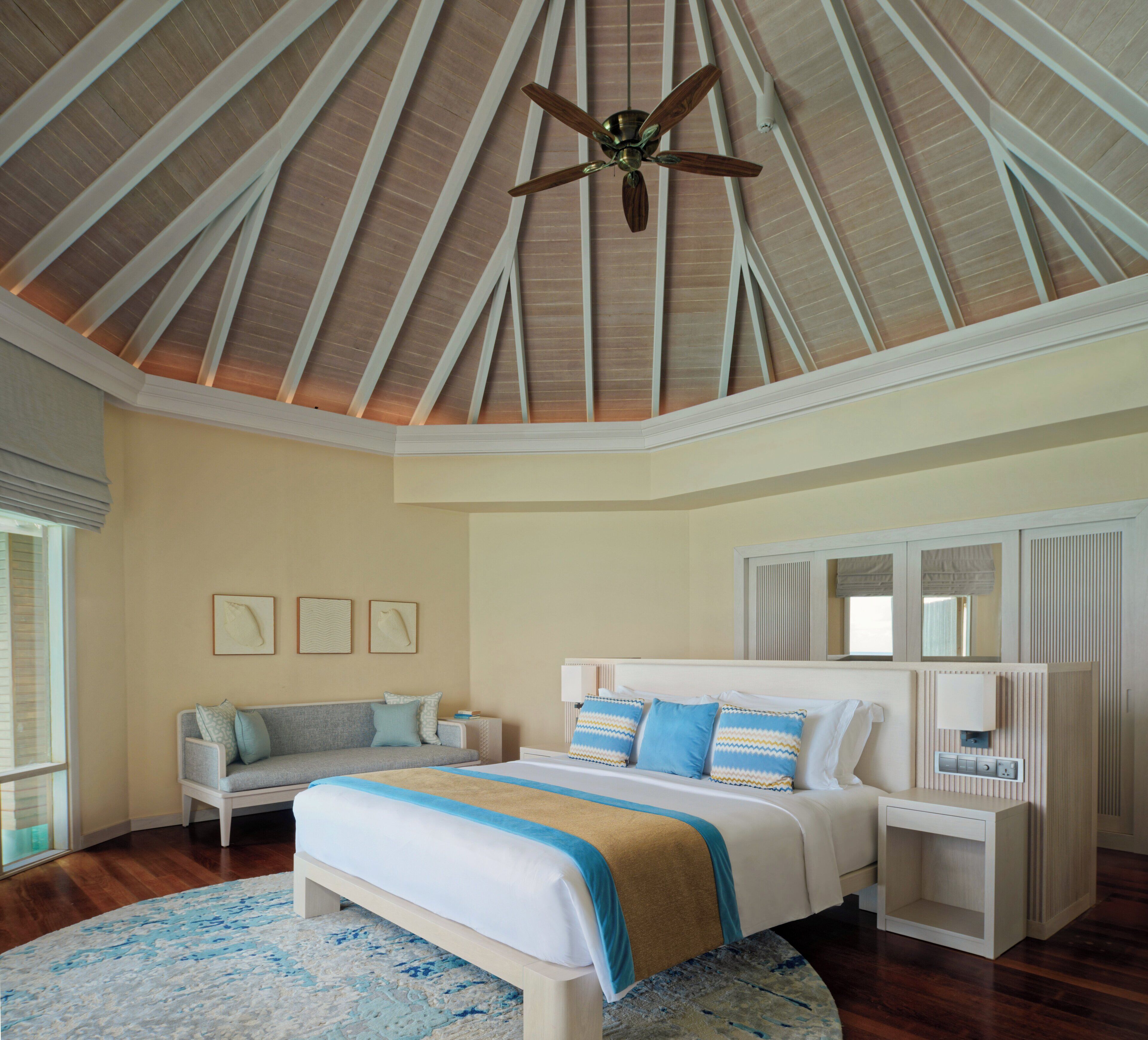 A spacious bedroom with a large bed, a ceiling fan, and a view of the sky through the skylight.