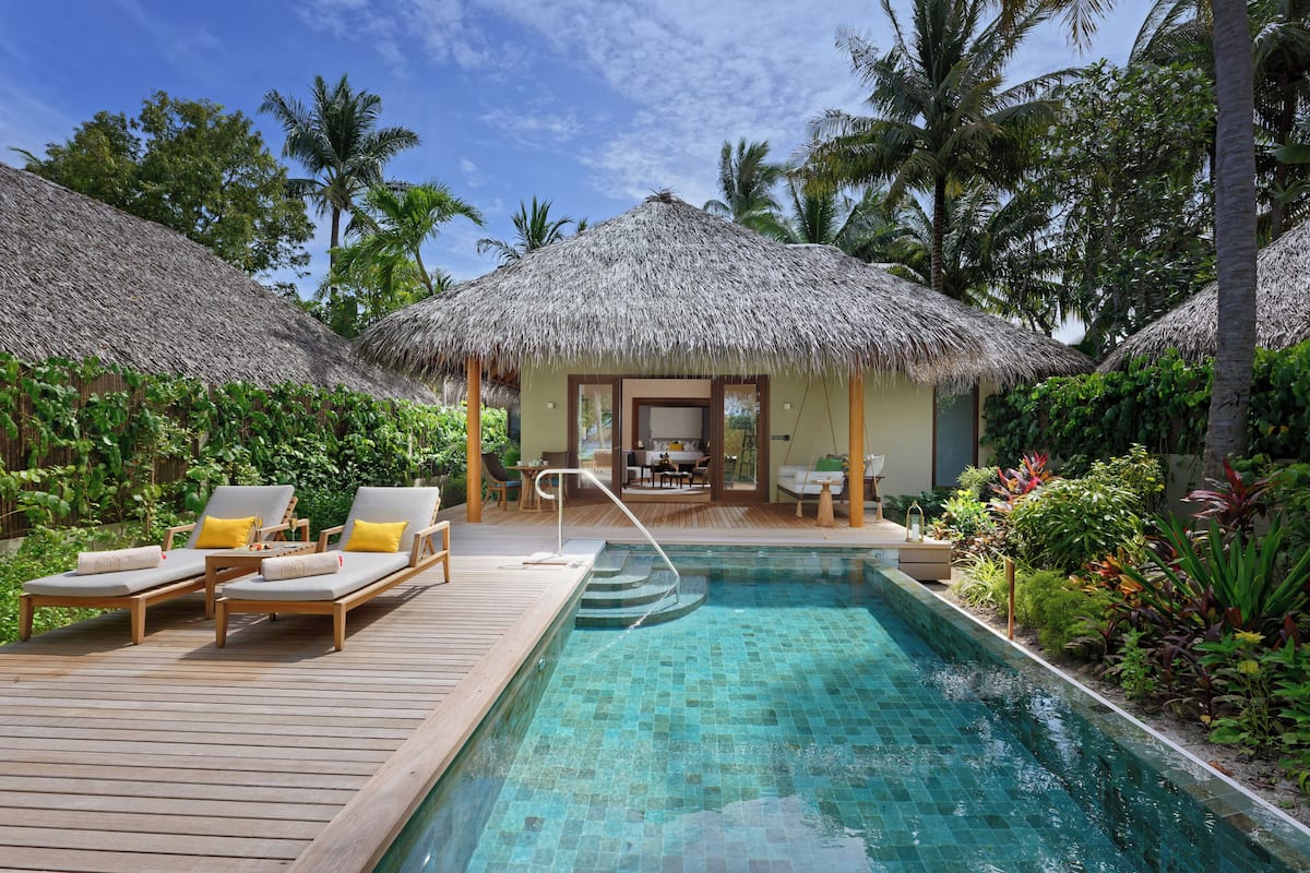 A pool area with lounge chairs, a thatched-roof structure, and lush greenery.