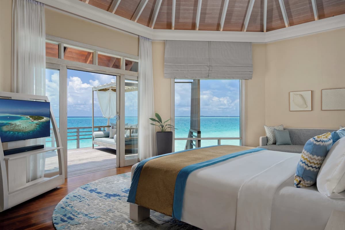 A bedroom with a large bed, a TV, and a view of the ocean.