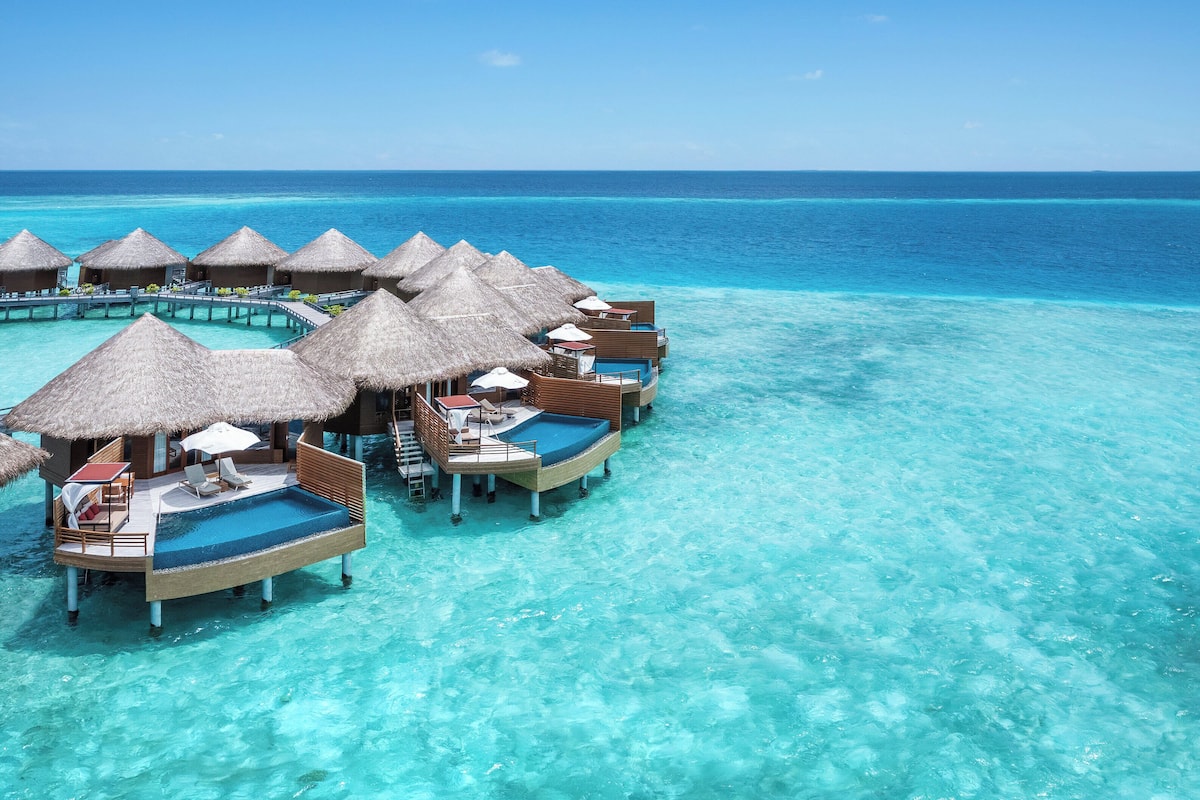 Overwater bungalows with thatched roofs and lounge chairs, connected by a bridge.