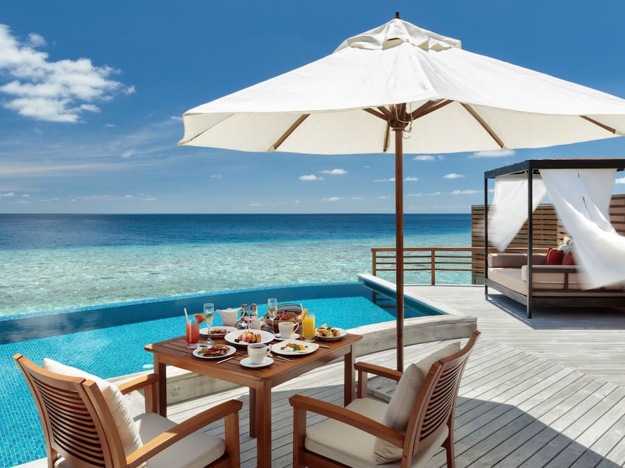 A wooden deck with a table set for breakfast overlooking a clear blue ocean.