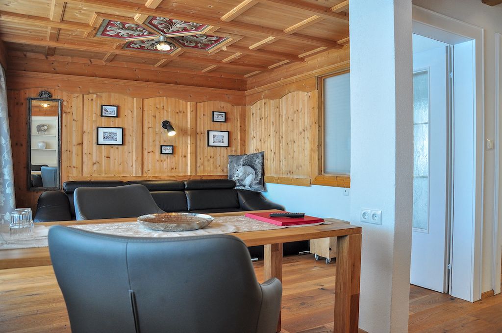 Ein gemütliches Zimmer mit Holzwänden und -decken, einer Couch, einem Esstisch mit Stühlen und gerahmten Bildern an der Wand.