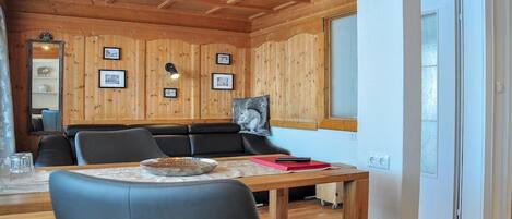 Ein gemütliches Zimmer mit Holzwänden und -decken, einer Couch, einem Esstisch mit Stühlen und gerahmten Bildern an der Wand.