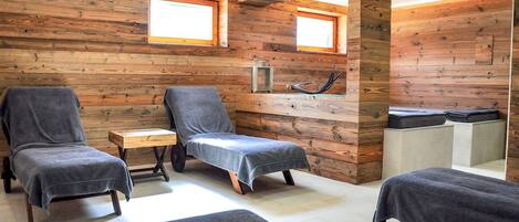 A wooden room with two massage chairs, a small table, and a bench.