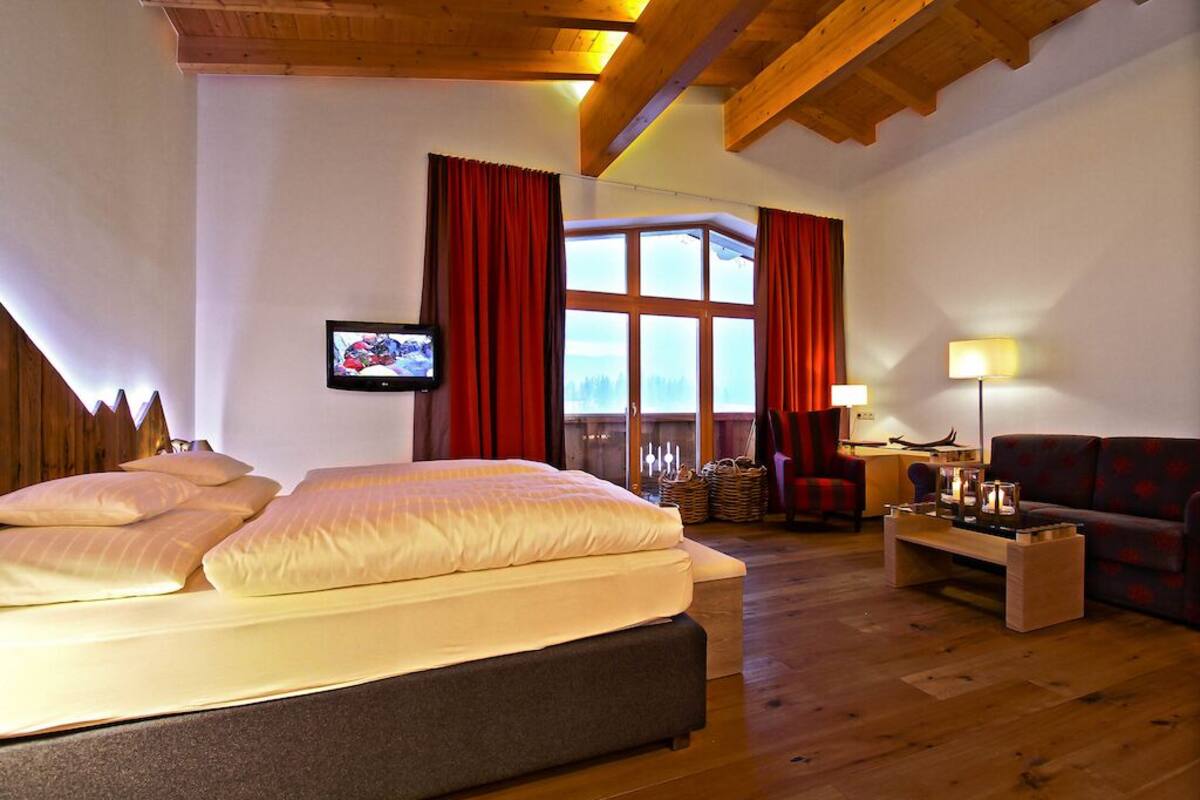 Ein Hotelzimmer mit einem großen Bett, einer Couch, einem Fernseher und einem Fenster mit Vorhängen.
