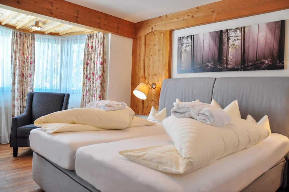 Ein Hotelzimmer mit zwei Betten, Holzvertäfelung, einem Waldgemälde und einem Sessel.